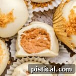 Gingerbread truffles in white paper cups with gingersnap cookies crumbles sprinkles on top of the white chocolate coating. One truffle has a bite out of it.