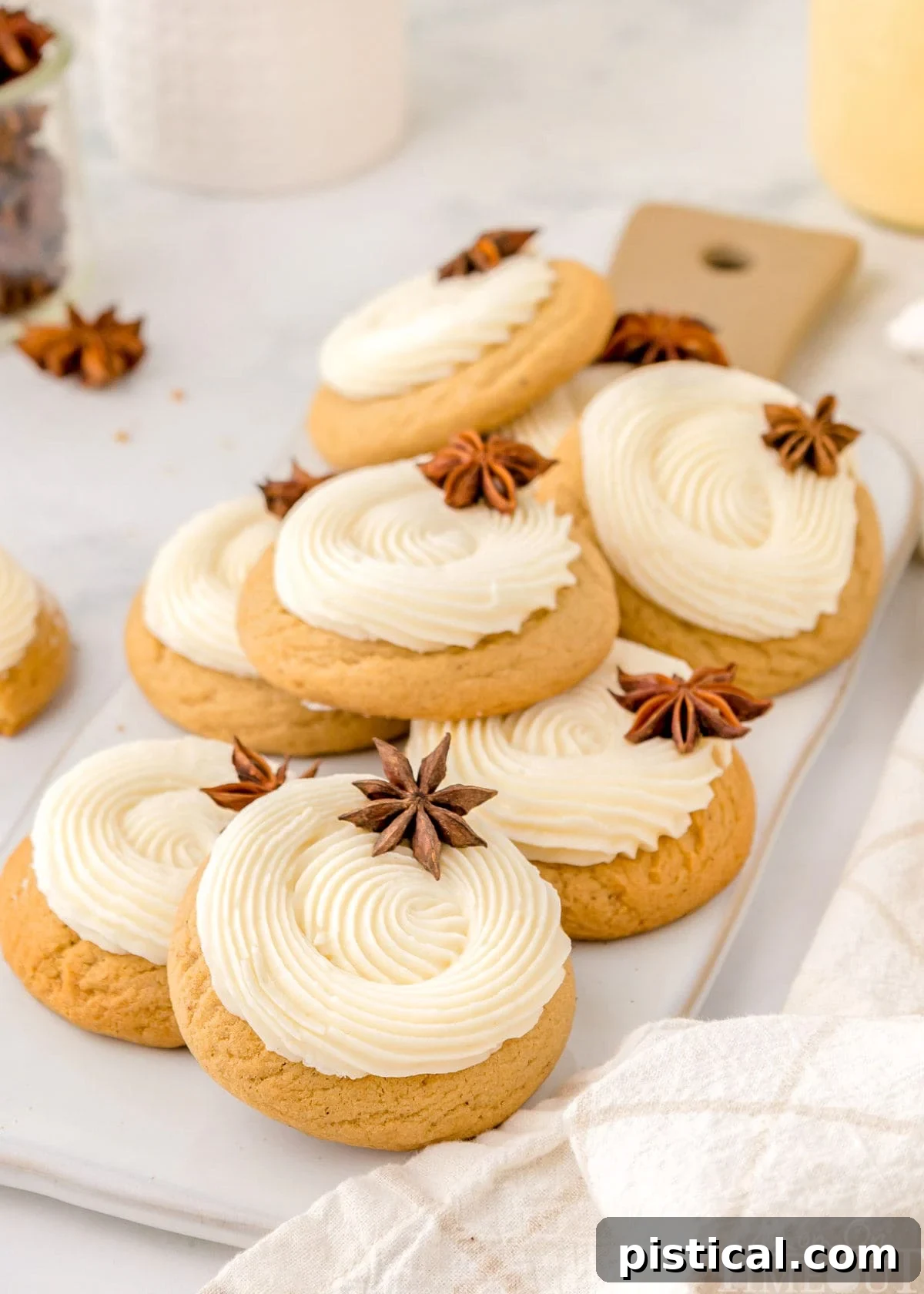 Eight beautifully frosted eggnog cookies, each elegantly topped with a delicate star anise, are artfully arranged on a long, rectangular wooden serving board. The display exudes warmth and festive charm, perfect for holiday entertaining.
