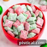red bowl filled with red and green puppy chow. the bowl is on a white surface which christmas decorations in the background.