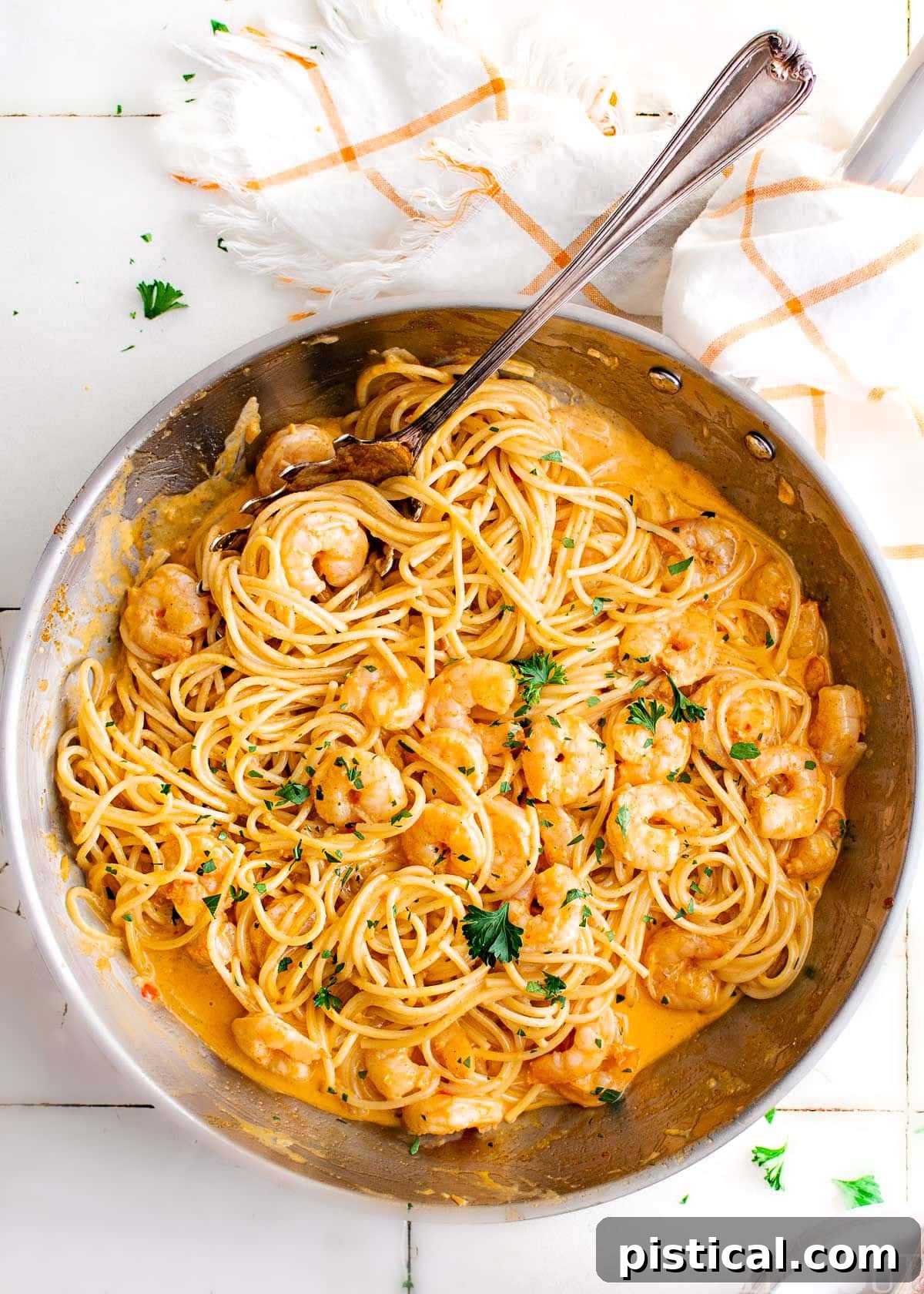Top-down view of Bang Bang Shrimp Pasta in a large skillet, garnished with fresh parsley, sitting on a countertop next to a white and orange kitchen towel.