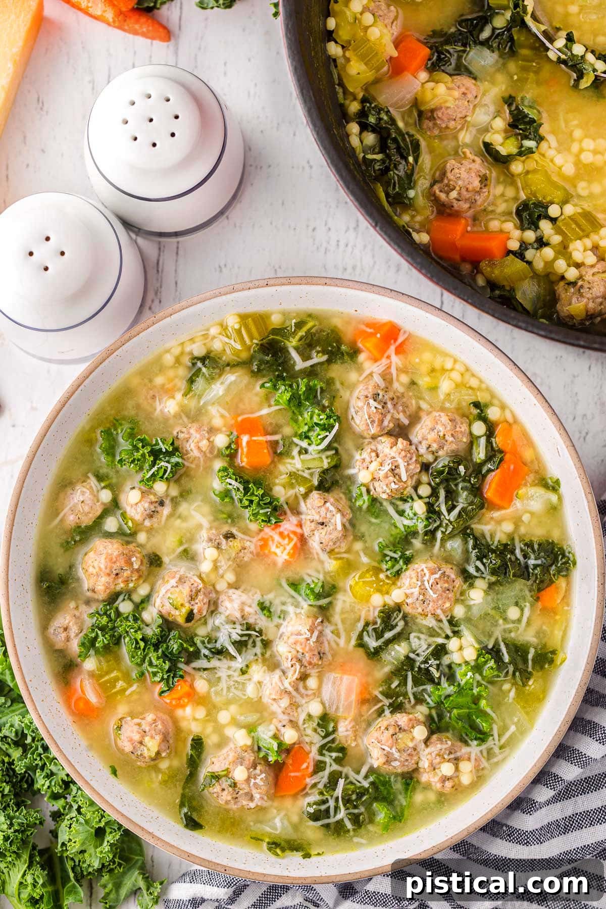 top down view of bowl of italian wedding soup topped with freshly grated parmesan cheese. the pot of soup is next to it.