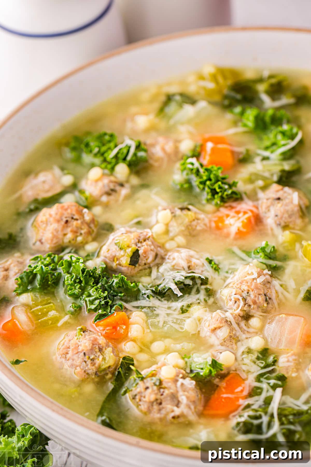 close up look at italian wedding soup in a round bowl. the soup has been topped with Parmesan cheese.