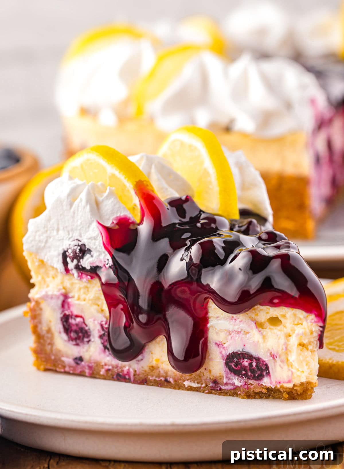 Luscious Lemon Blueberry Cheesecake 6 side view of lemon blueberry cheesecake topped with blueberry pie filling and fresh whipped cream. the rest of the cheesecake can be seen in the background.