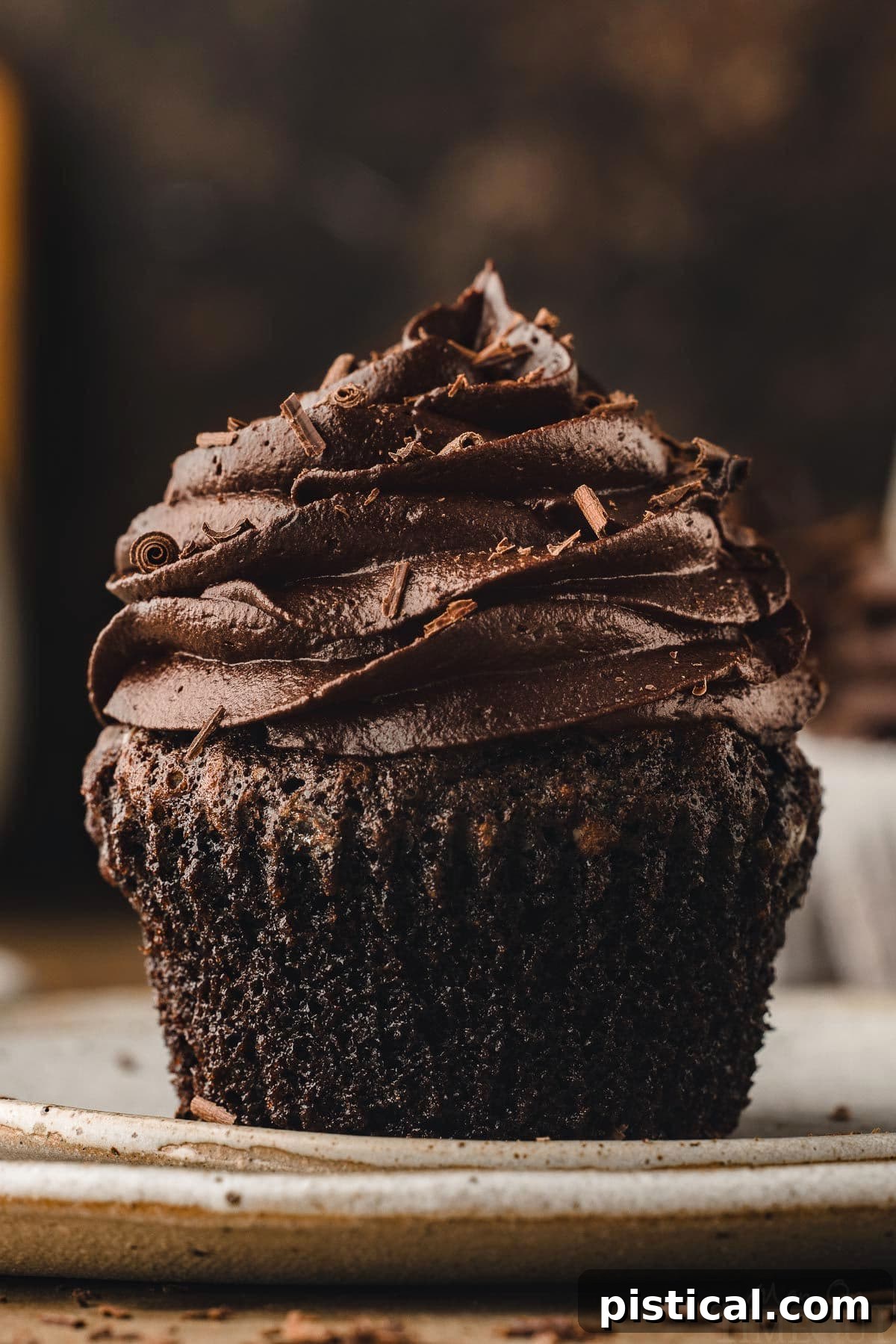 A perfectly moist chocolate cupcake, removed from its liner and resting on a white plate, adorned with a smooth, rich chocolate buttercream frosting. This image highlights the luscious texture and inviting appearance of the ultimate chocolate cupcake.