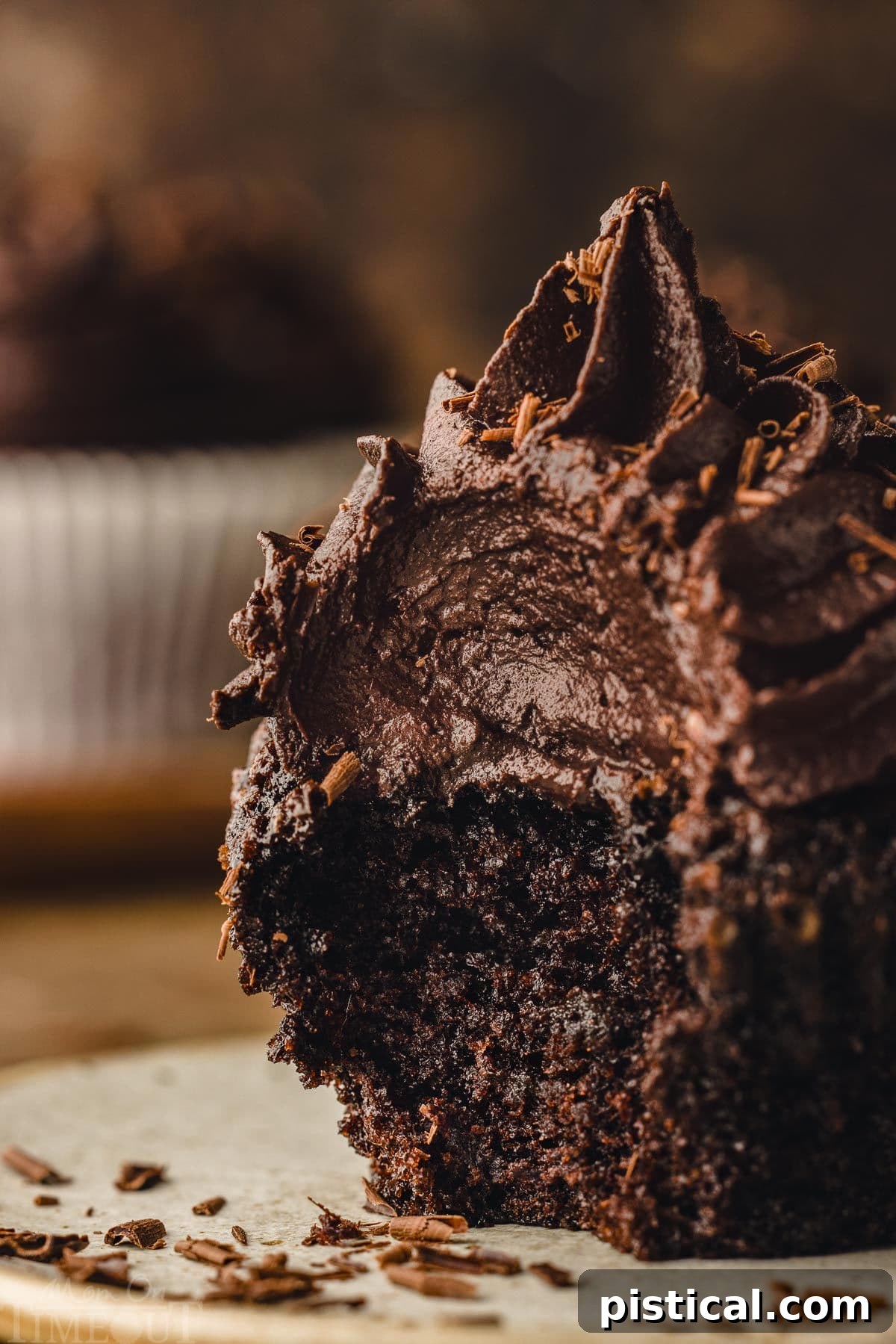 A chocolate cupcake with a bite taken out of it rests on a small plate. The frosting is generously piled high, appearing rich and creamy, highlighting the indulgent nature of the dessert.