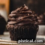 chocolate cupcake with liner removed sitting on white plate. cupcake has been topped with a chocolate buttercream frosting.