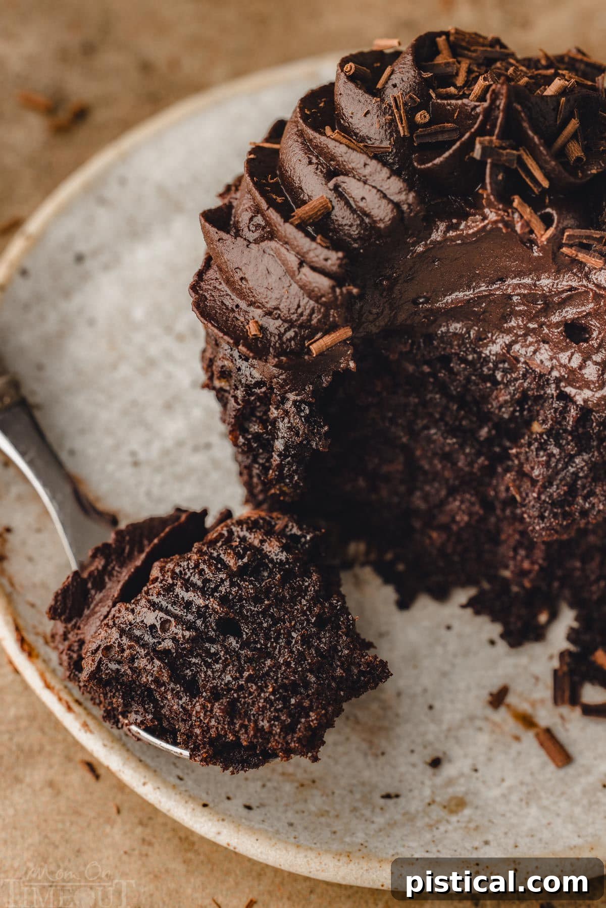 A fork rests on a white plate beside a chocolate cupcake that has had a bite taken out of it. A piece of the cupcake and frosting is on the fork, highlighting its moist and rich texture.
