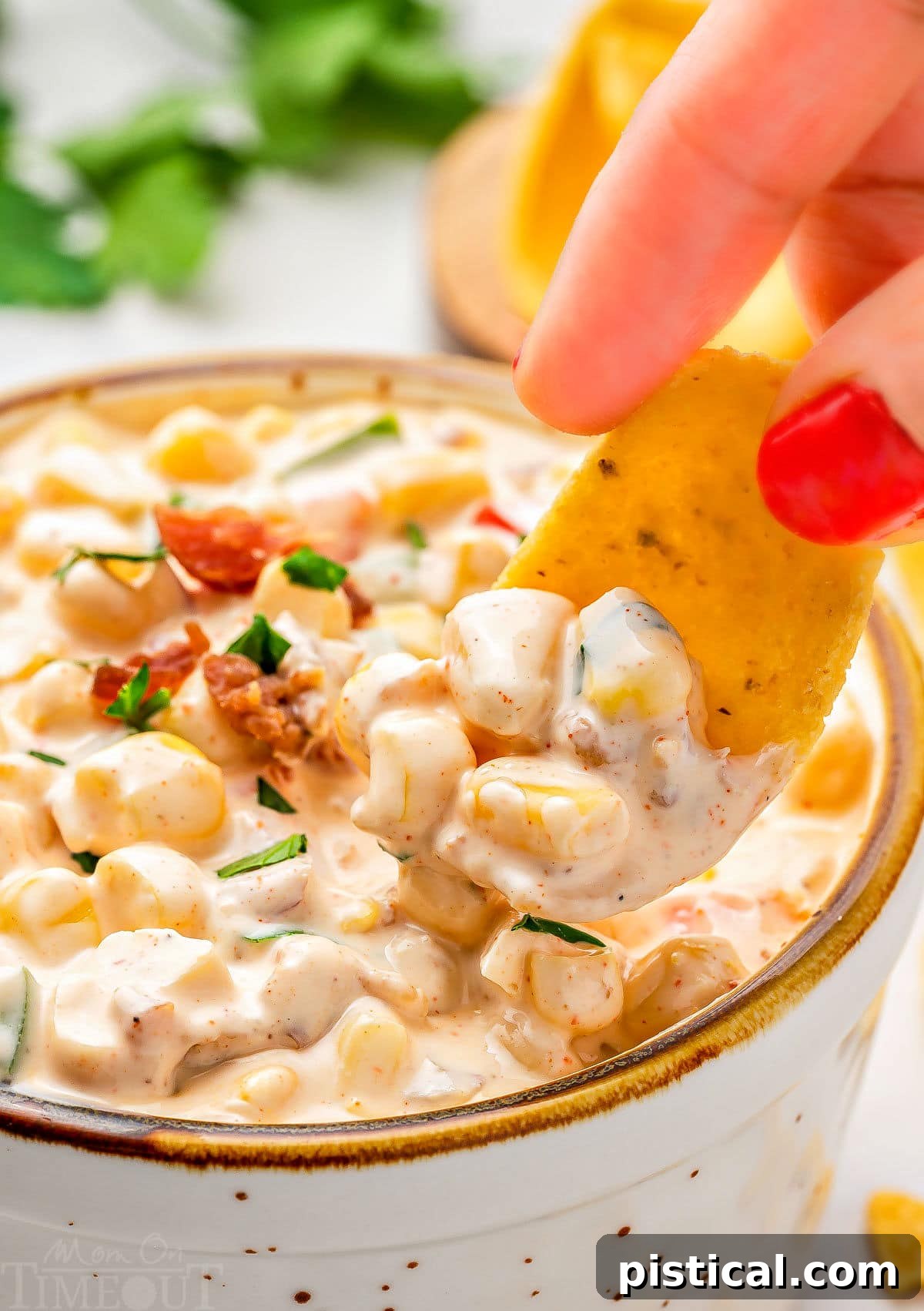 close up look at a frito scoop picking up a bit of corn dip from a small bowl. the dip has been topped with bacon and parsley. 