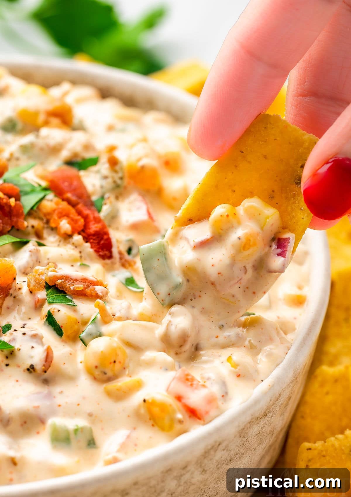 close up look at a frito scoop picking up a bit of corn dip from a small bowl. the dip has been topped with bacon and parsley.