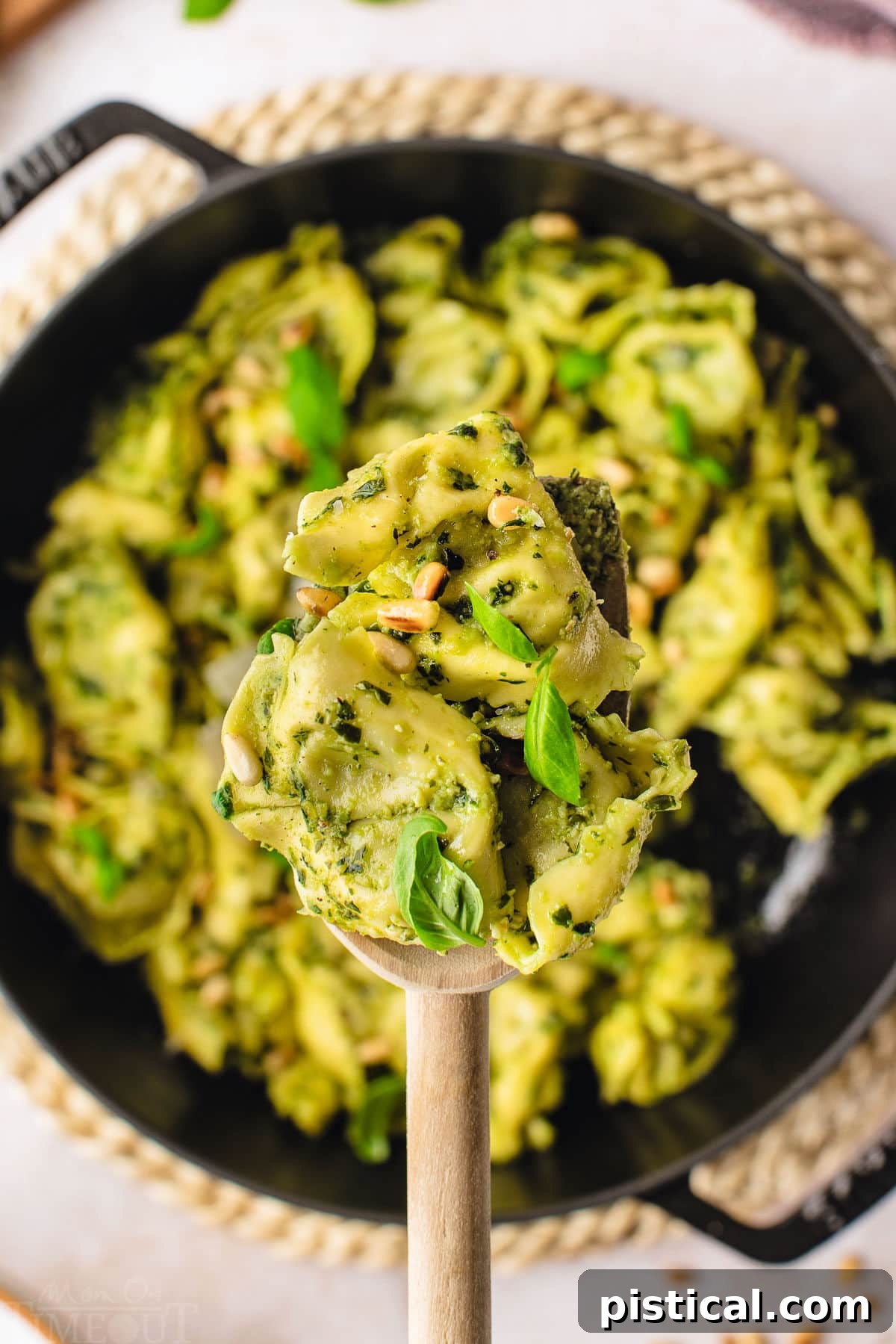 Close-up of a spoonful of pesto tortellini lifted from a cast iron skillet, showcasing the rich green pesto coating the pasta.