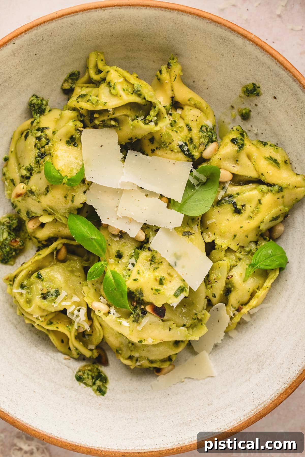 Top-down shot of a bowl of Pesto Tortellini, beautifully garnished with fresh basil leaves and a generous dusting of Parmesan cheese.