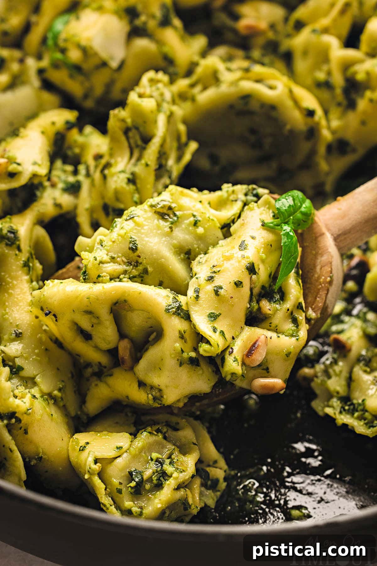 Wooden spoon resting in a cast iron skillet filled with Pesto Tortellini, ready to be served.