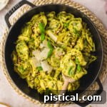 Top-down look at pesto tortellini in a black cast iron skillet. Made with fresh basil pesto and topped with Parmesan and basil.