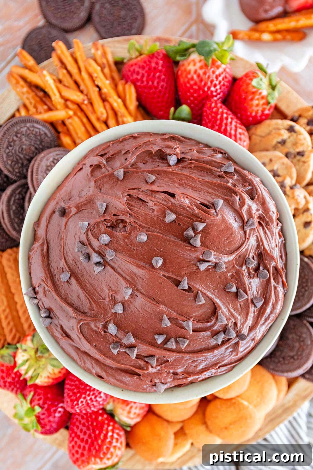 close up top down shot of a bowl of brownie batter dip surrounded by dippers including fresh strawberries, nilla wafers, pretzels and cookies.