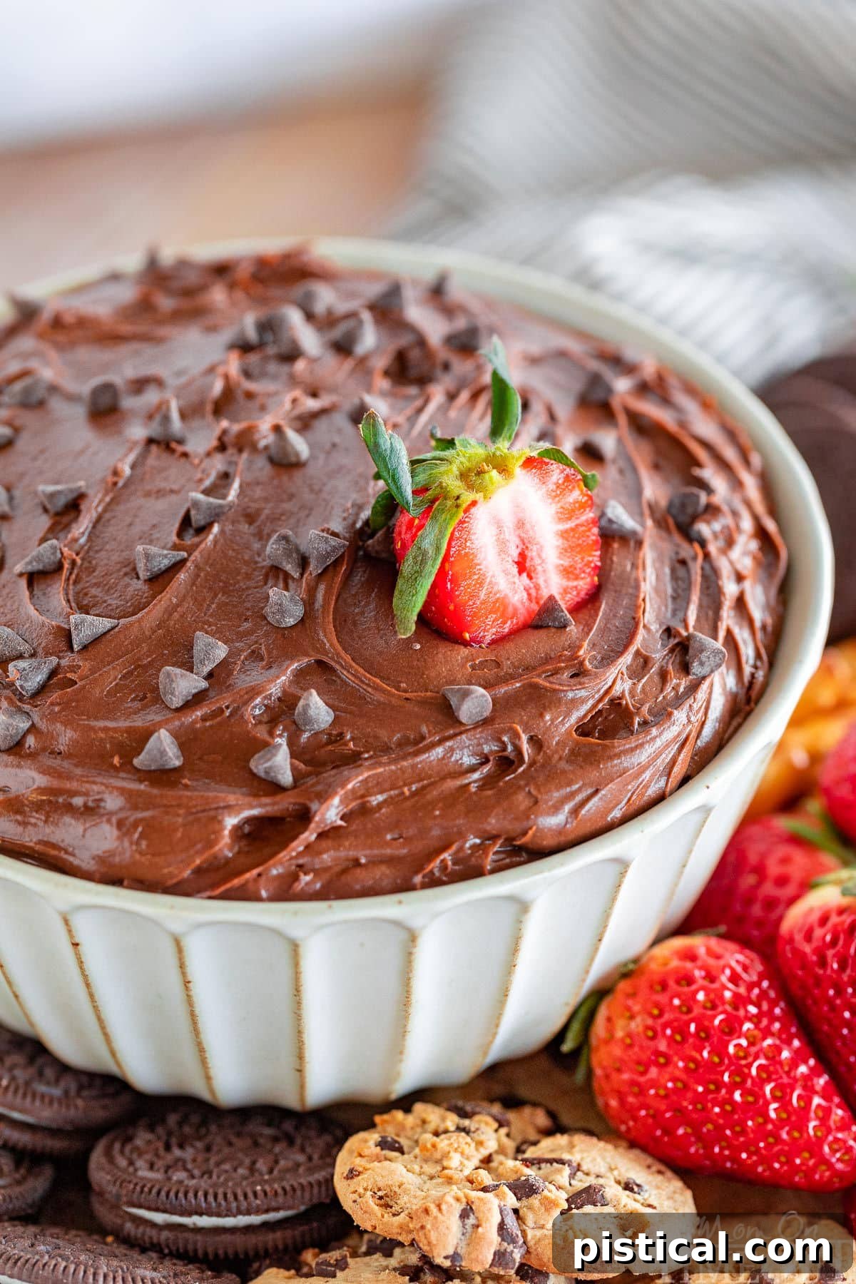 close up of bowl of brownie dip with a half strawberry stuck in the top along with a scattering of mini chocolate chips.
