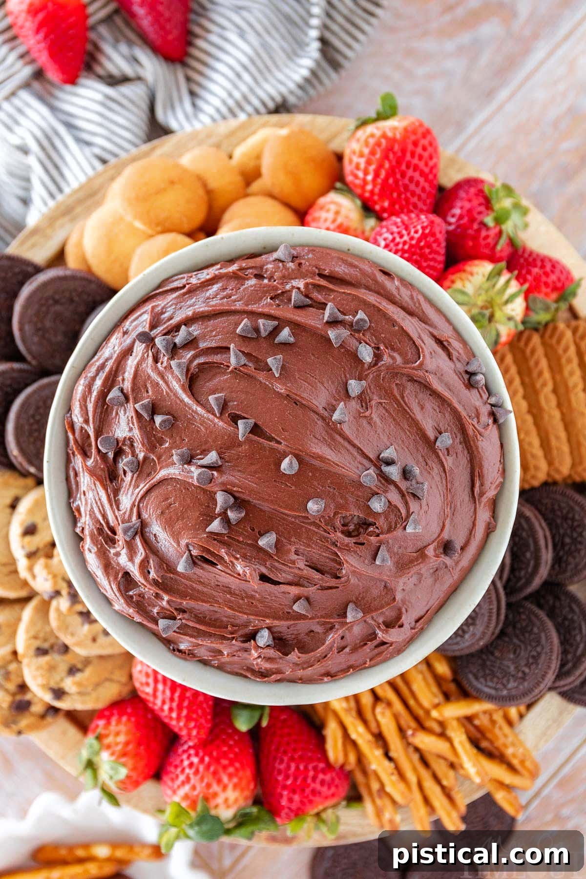 top down shot of a bowl of brownie batter dip surrounded by dippers including fresh strawberries, nilla wafers, pretzels and cookies.