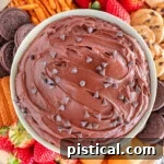 close up top down shot of a bowl of brownie batter dip surrounded by dippers including fresh strawberries, nilla wafers, pretzels and cookies.