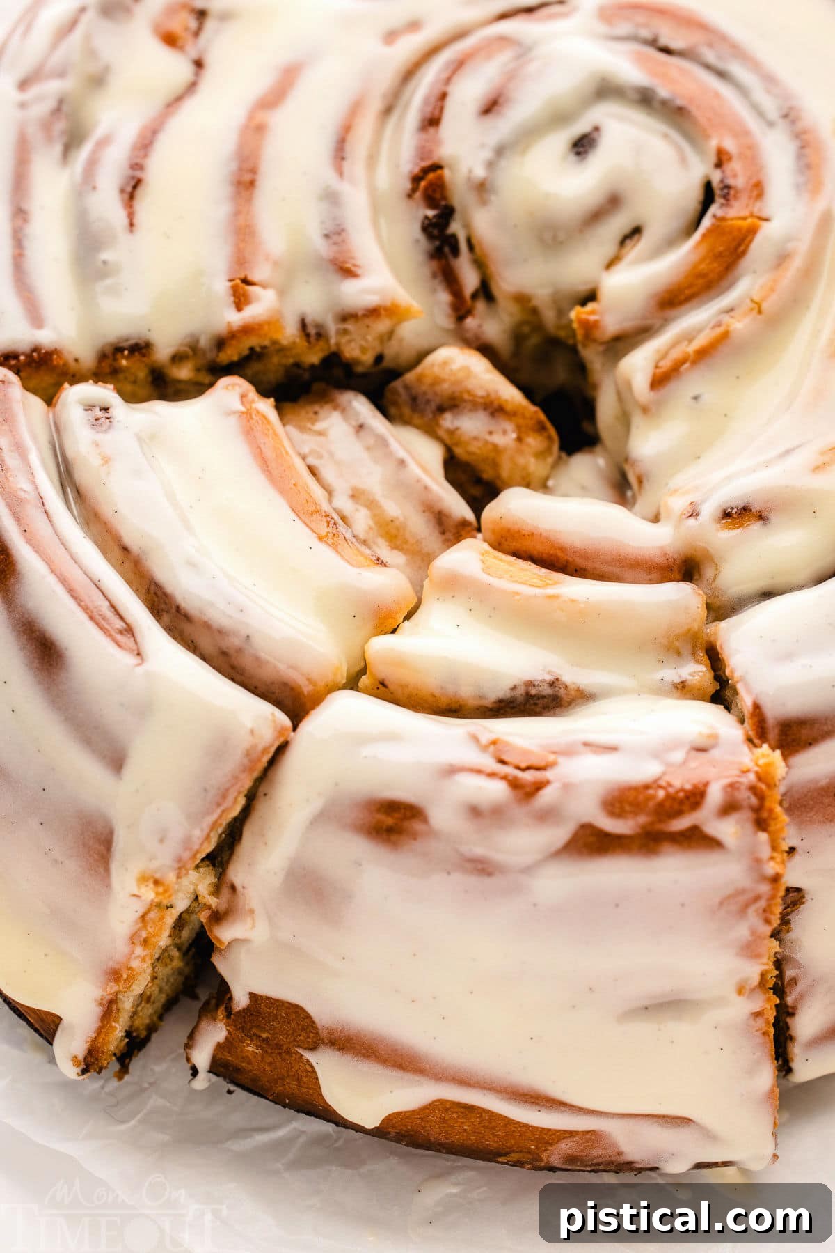 Close-up, top-down view of a generously glazed Giant Cinnamon Roll Cake with two perfect slices already cut, revealing the irresistible swirls.