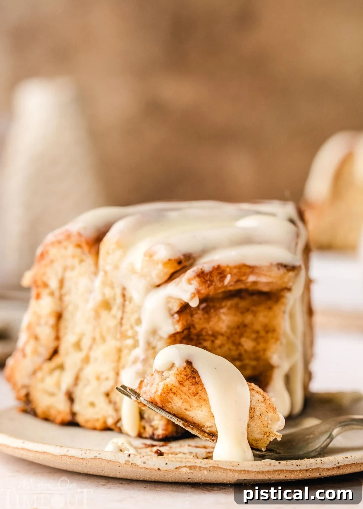 A perfectly sliced piece of Giant Cinnamon Roll Cake, beautifully plated on a small white dish, with the rich cream cheese glaze generously drizzled over the top. A fork has just taken a delightful bite from the tip of the slice.