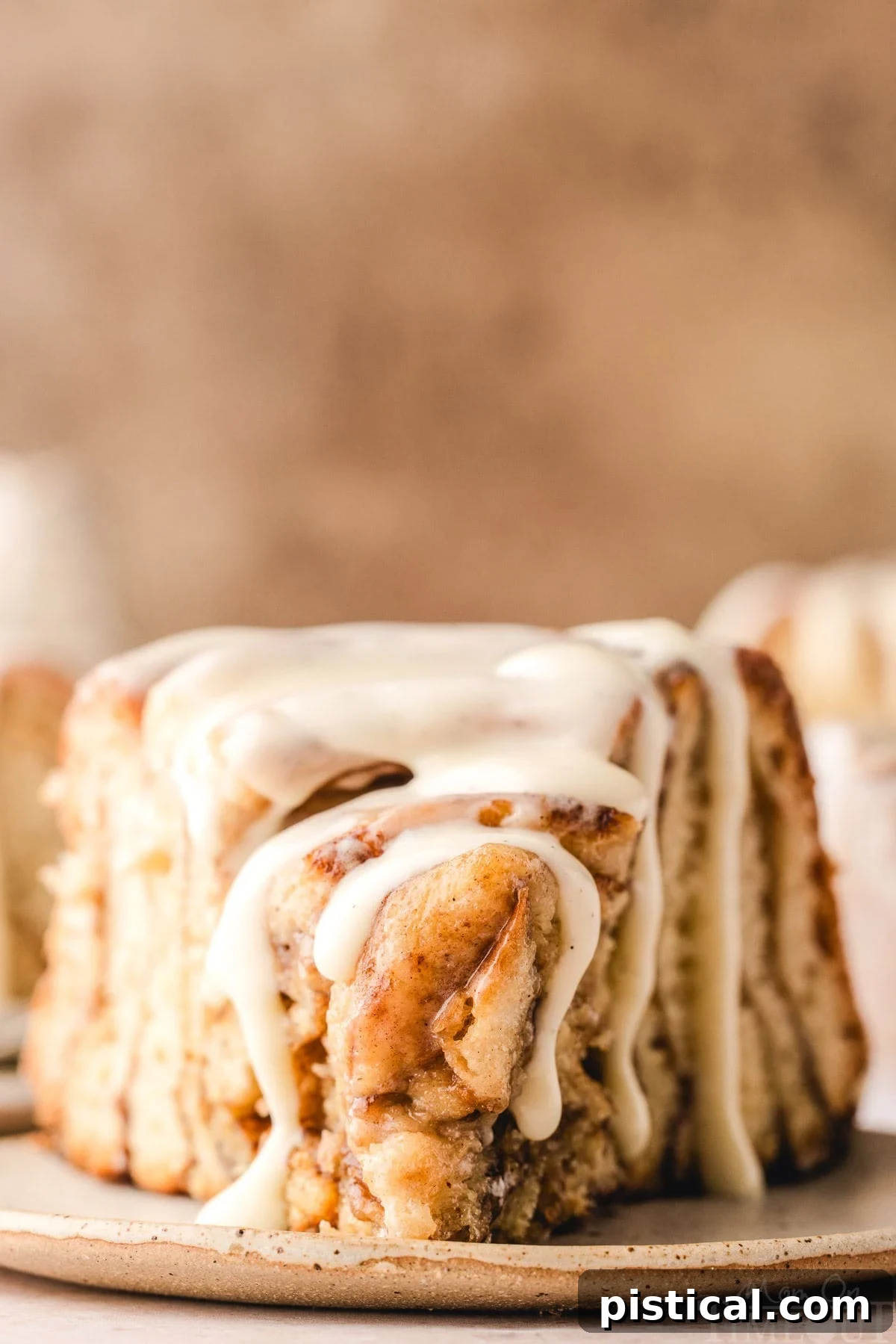 A beautiful slice of Giant Cinnamon Roll Cake, perfectly plated on a small white dish, showcasing the distinct swirls of cinnamon and sugar. The cake is generously drizzled with a smooth cream cheese glaze.