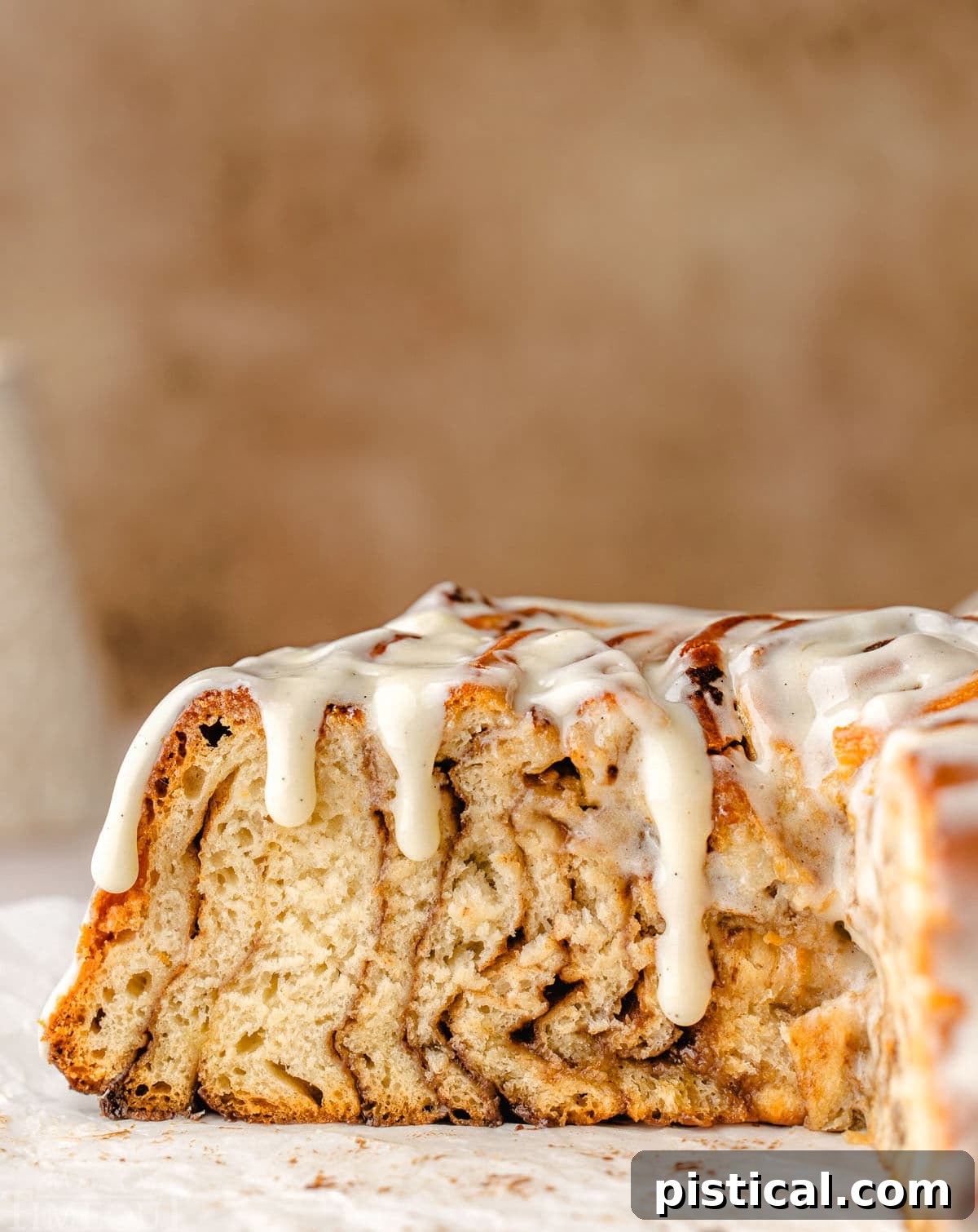 A stunning cross-sectional view of the Giant Cinnamon Roll Cake, clearly showing all the beautiful, defined swirls of cinnamon sugar filling, with the luscious cream cheese glaze gracefully dripping down the sides of the cake.