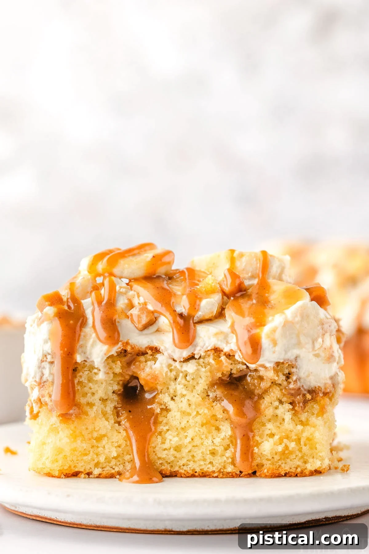 Dreamy Banoffee Poke Cake 2 A beautifully presented slice of Banoffee Poke Cake on a white plate, adorned with whipped cream, banana slices, and a drizzle of dulce de leche sauce.