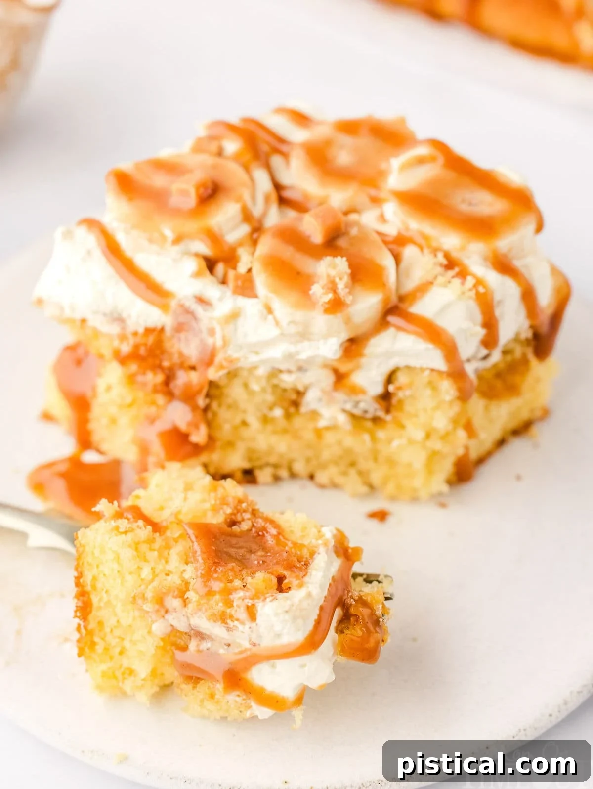Dreamy Banoffee Poke Cake 5 A forkful of Banoffee Poke Cake sits next to the remaining slice on a small, round white plate.