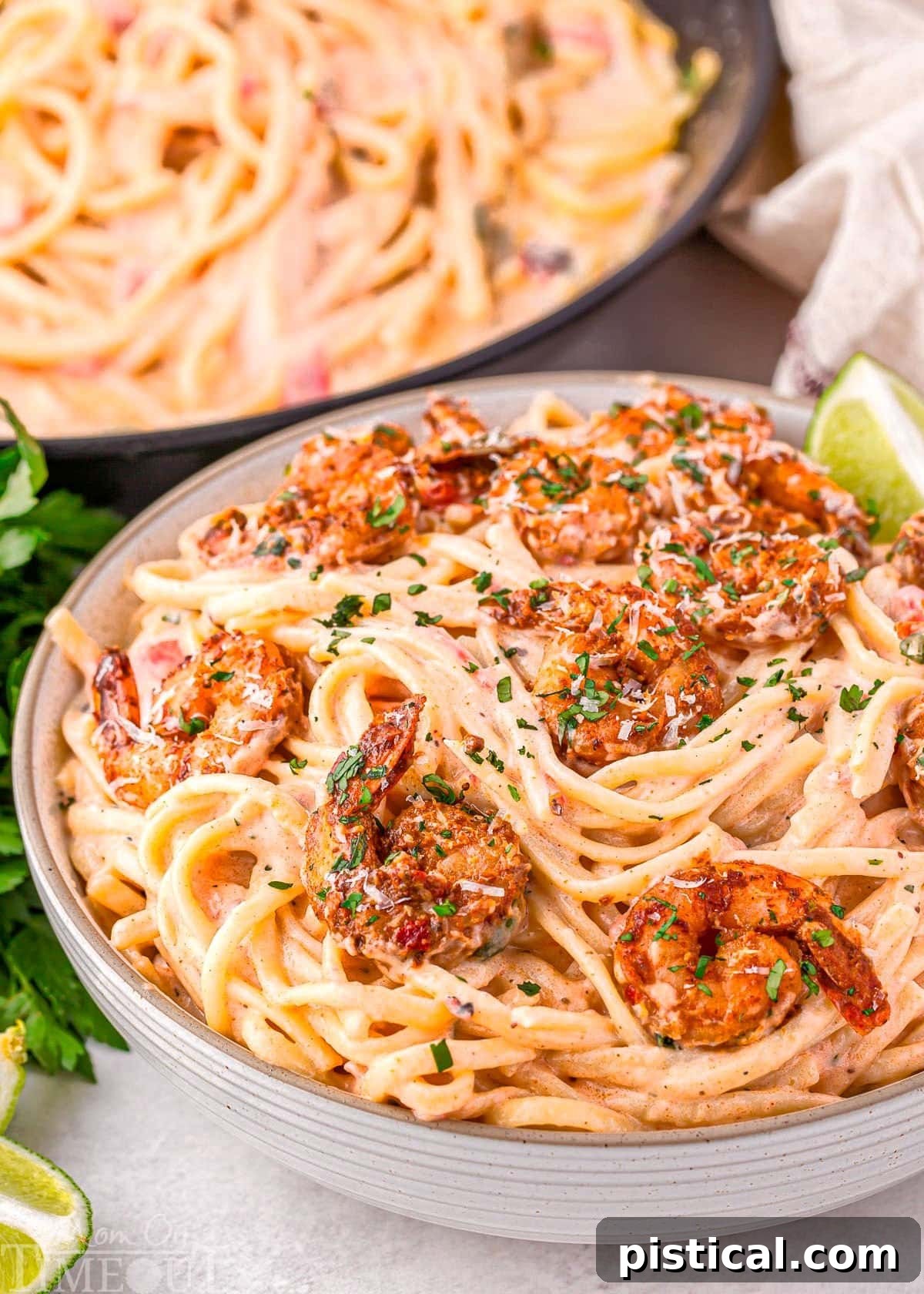 Close up look at bowl of creamy Cajun shrimp pasta recipe with a rich Parmesan cream sauce and topped with spicy crispy Cajun shrimp, garnished with fresh parsley.
