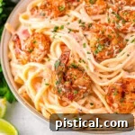 Close up look at bowl of cajun shrimp pasta recipe with a rich Parmesan cream sauce and topped with spicy shrimp and garnished with fresh parsley and Parmesan cheese.