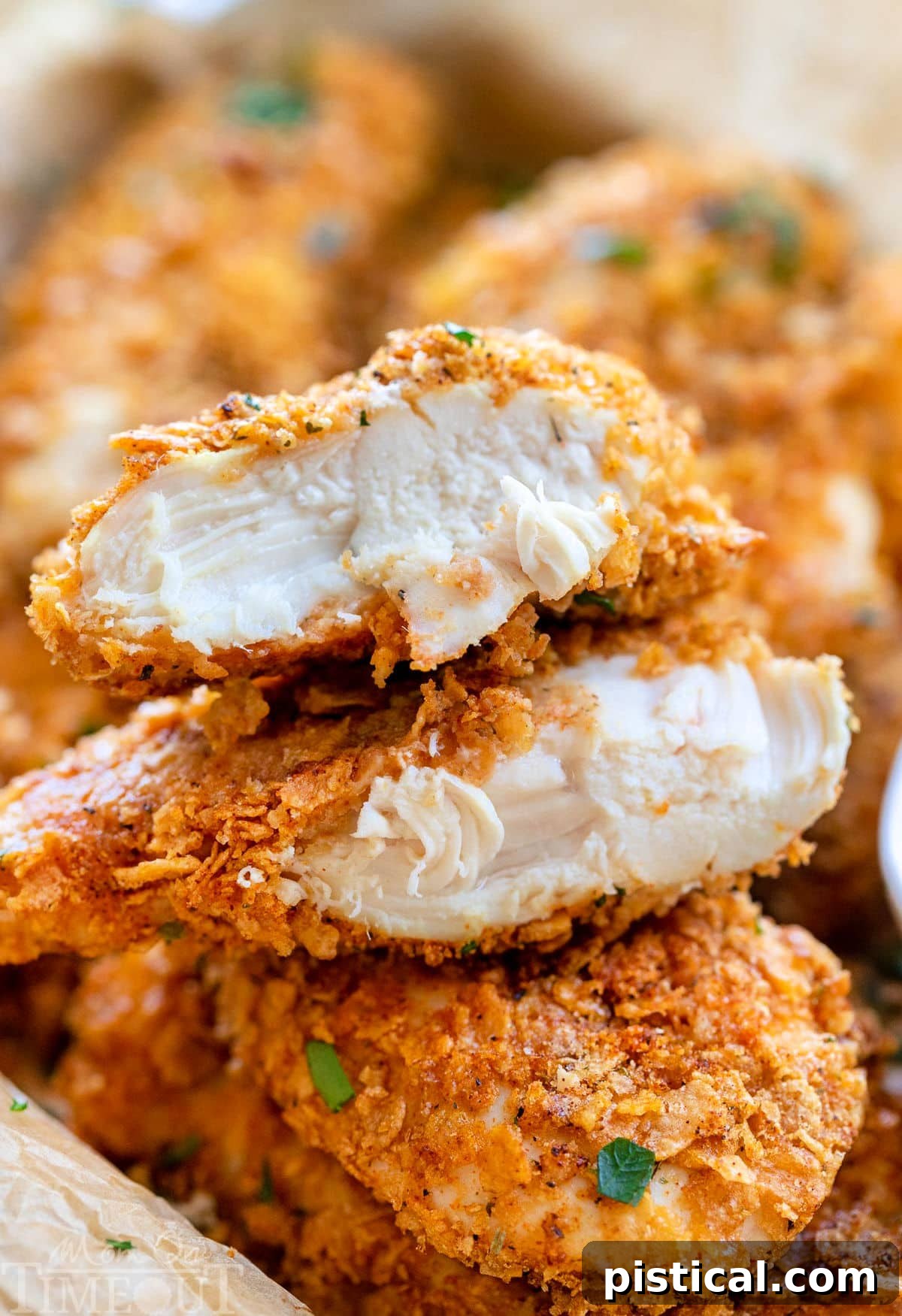 cornflake chicken in a pile with ranch dipping sauce. Top chicken tender is cut in half and stacked on each other showing the moist chicken and flavorful cornflake coating.