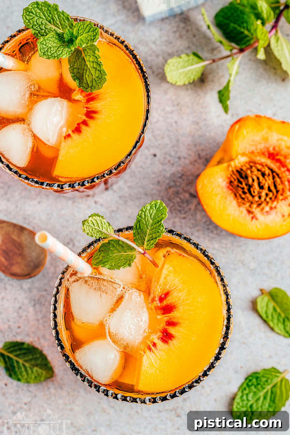 Sun-Kissed Peach Sip 3 Top-down view of two glasses of peach iced tea, garnished with mint and peach slices, each containing a paper straw. A halved peach with its pit rests beside the glasses.