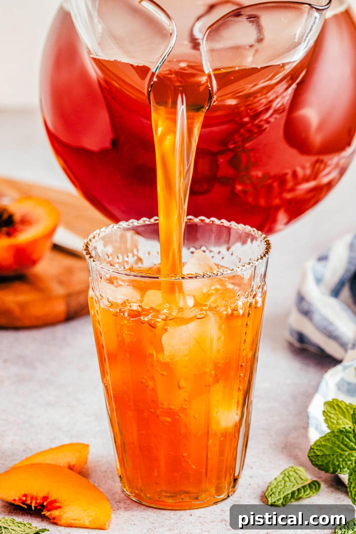 Sun-Kissed Peach Sip 4 A large pitcher of peach tea being poured into a tall glass filled with ice, creating a refreshing cascade.