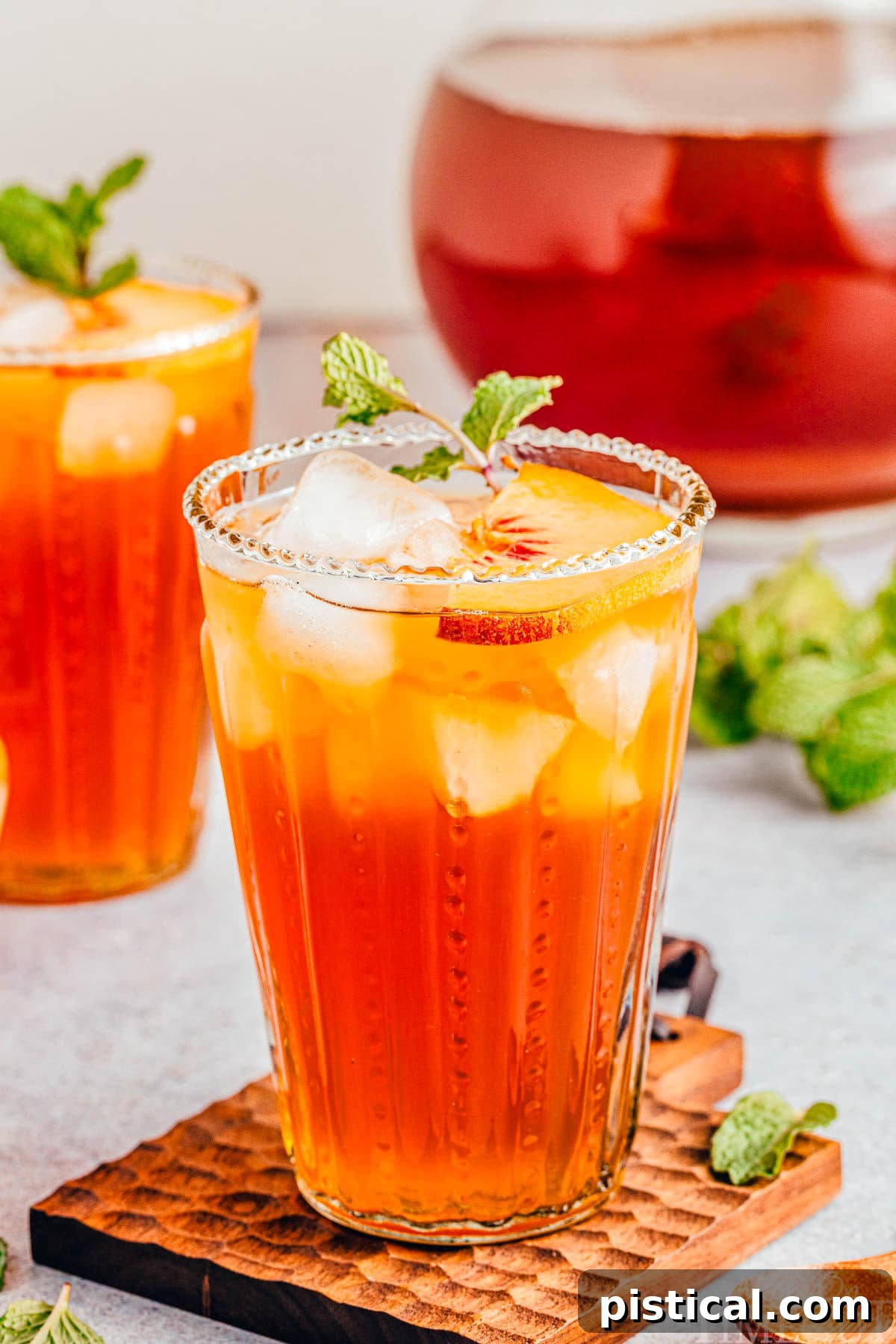 Sun-Kissed Peach Sip 9 A tall glass of refreshing peach tea positioned in front of a pitcher of tea and another glass, highlighting its inviting appeal.