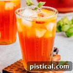 Tall glass of refreshing peach tea sitting in front of a pitcher of tea and another glass.