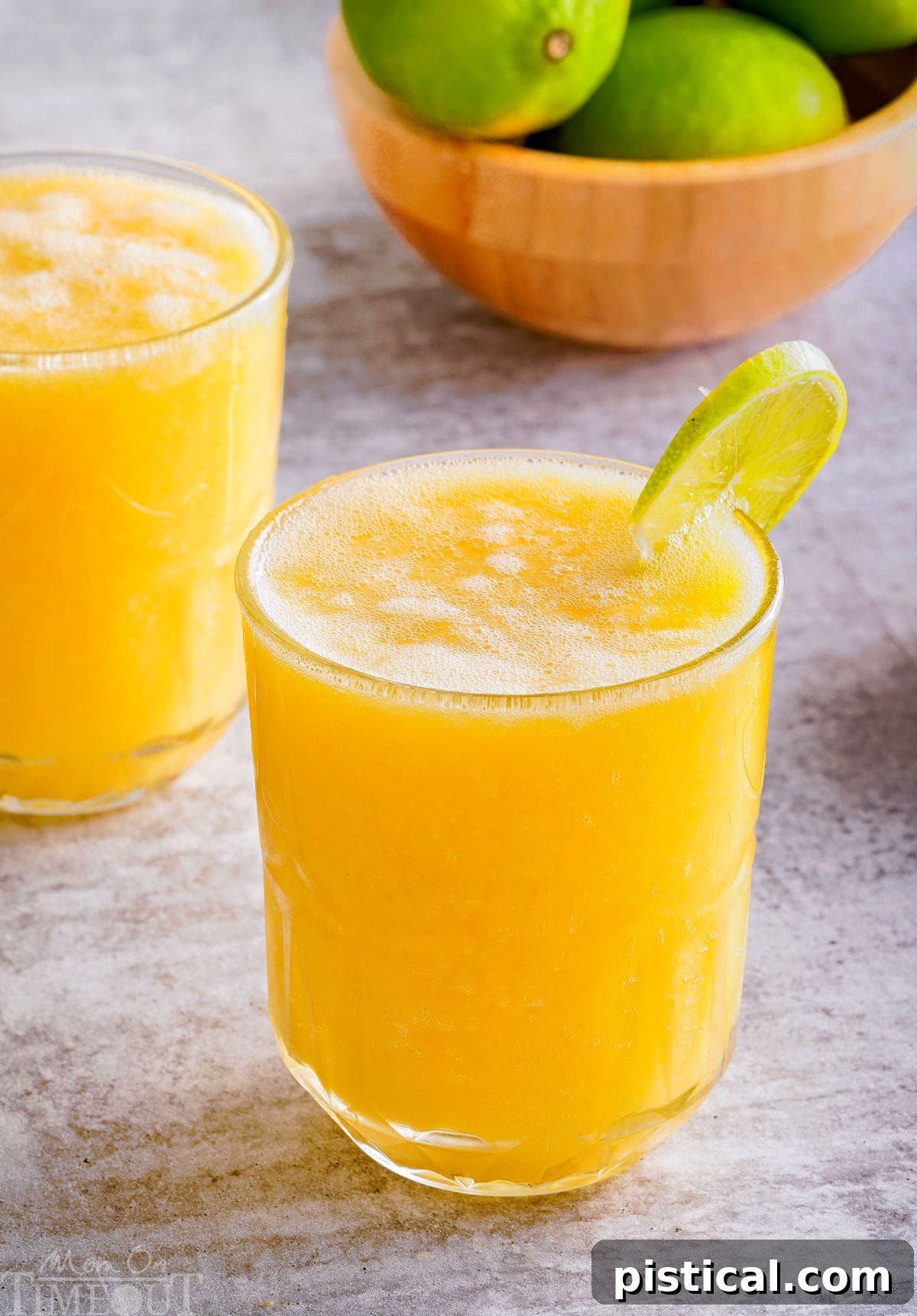A vibrant pineapple mango mocktail in a tall glass, garnished with a fresh lime wedge on the rim, evoking a tropical feel.