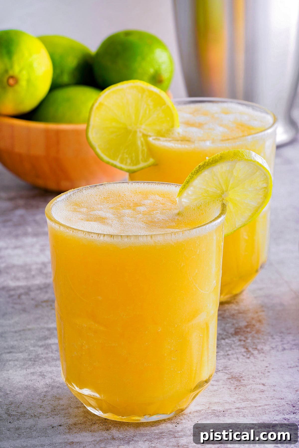Side view of two glasses filled with a refreshing pineapple mango mocktail, each elegantly garnished with a lime wedge on the rim, set against a bright background.