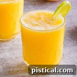 A vibrant pineapple mango mocktail in a tall glass, garnished with a fresh lime wedge on the rim, evoking a tropical feel.