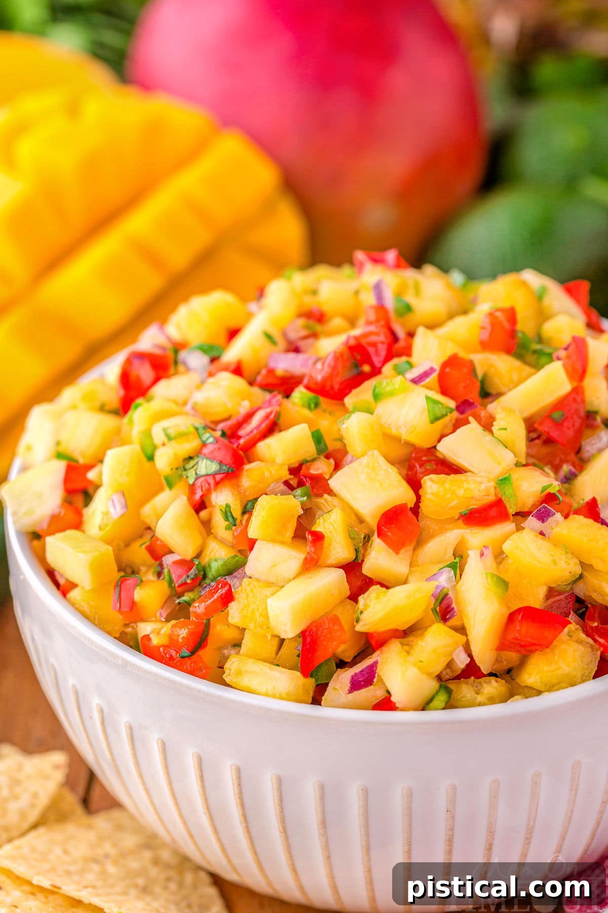 serving bowl filled with pineapple mango salsa ready to be enjoyed. Mangoes can be seen in the background.
