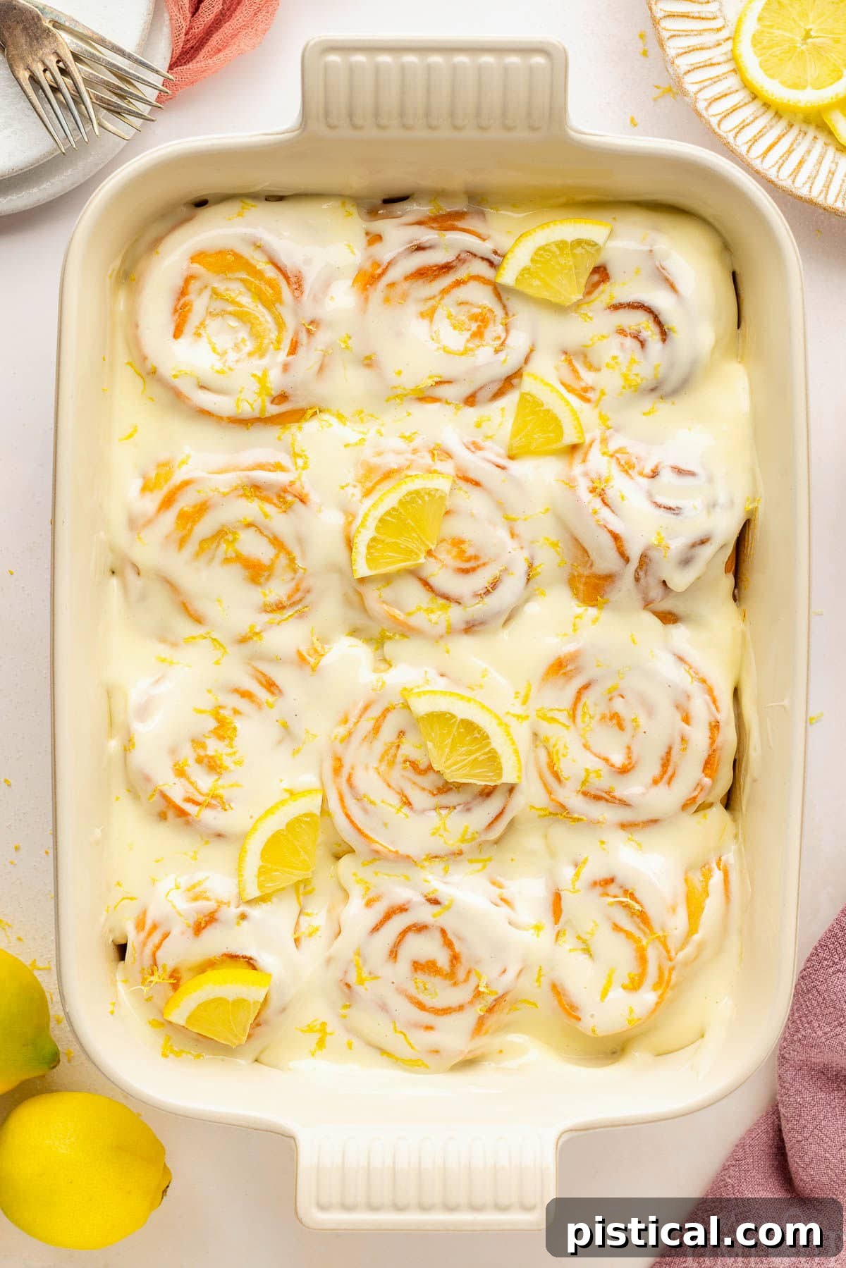 Zesty Lemon Swirls 2 An overhead view of a pan of lemon rolls on a white surface, freshly baked and glazed.