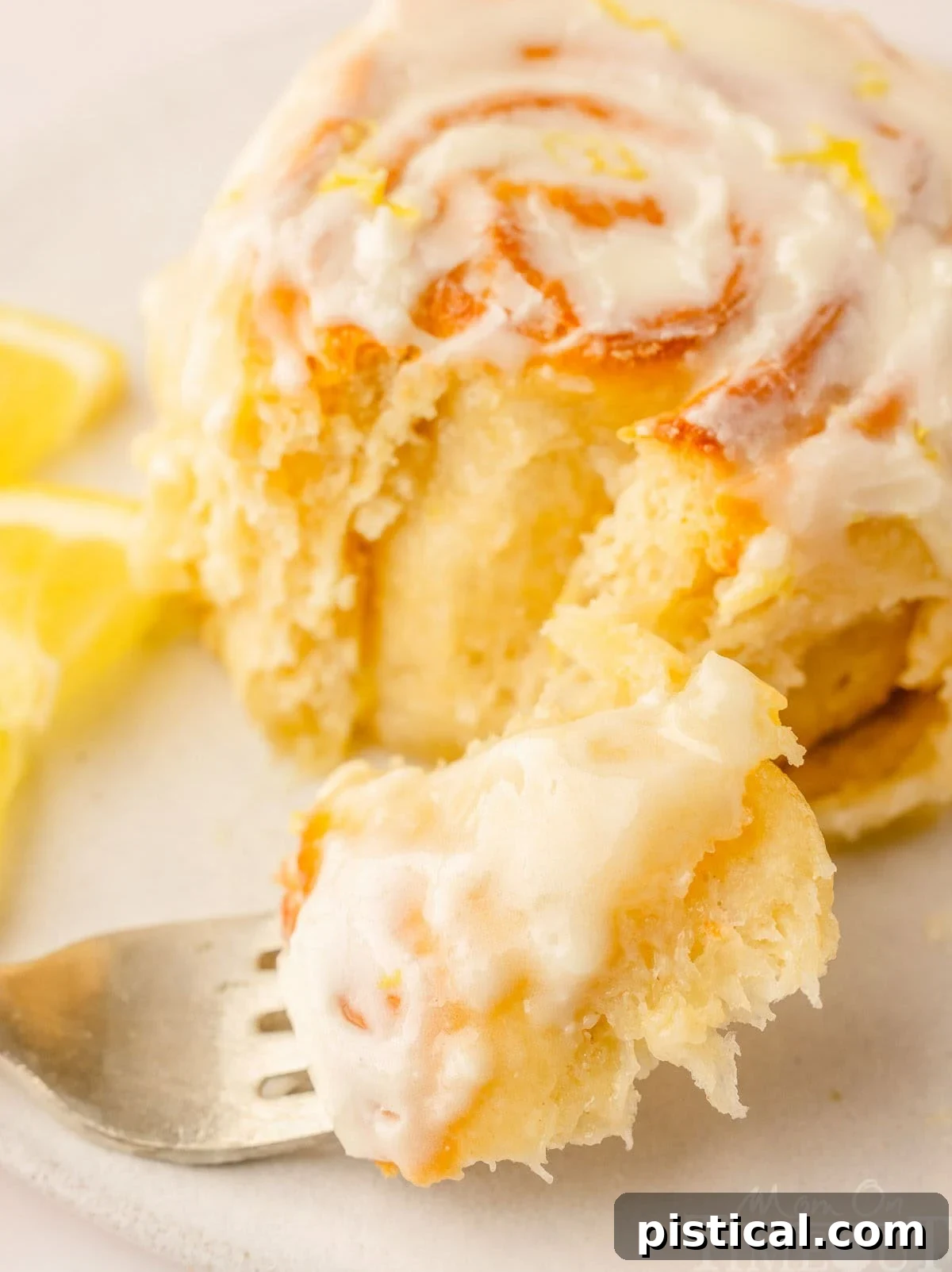 Zesty Lemon Swirls 3 A single lemon roll with a fork sitting on a white plate next to it, showing the soft interior.