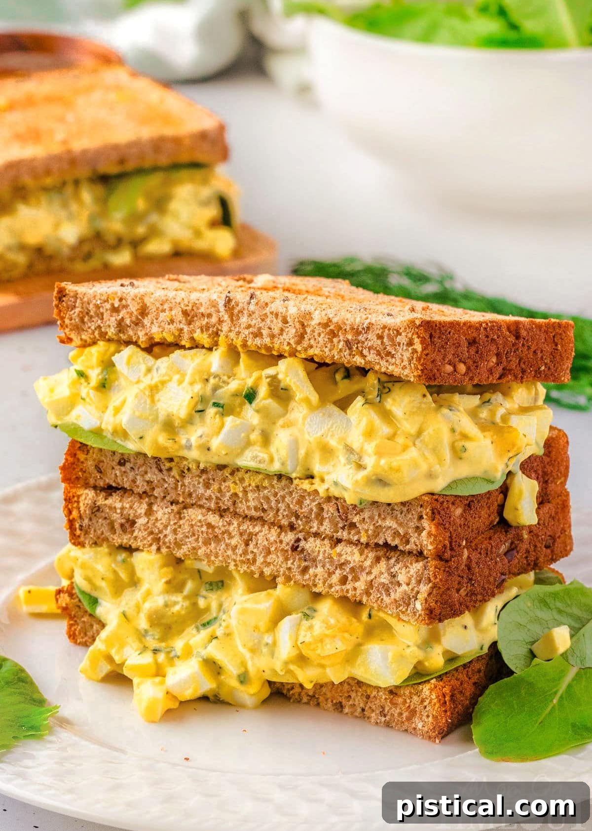 Two egg salad halves of a sandwich stacked on top of each other.