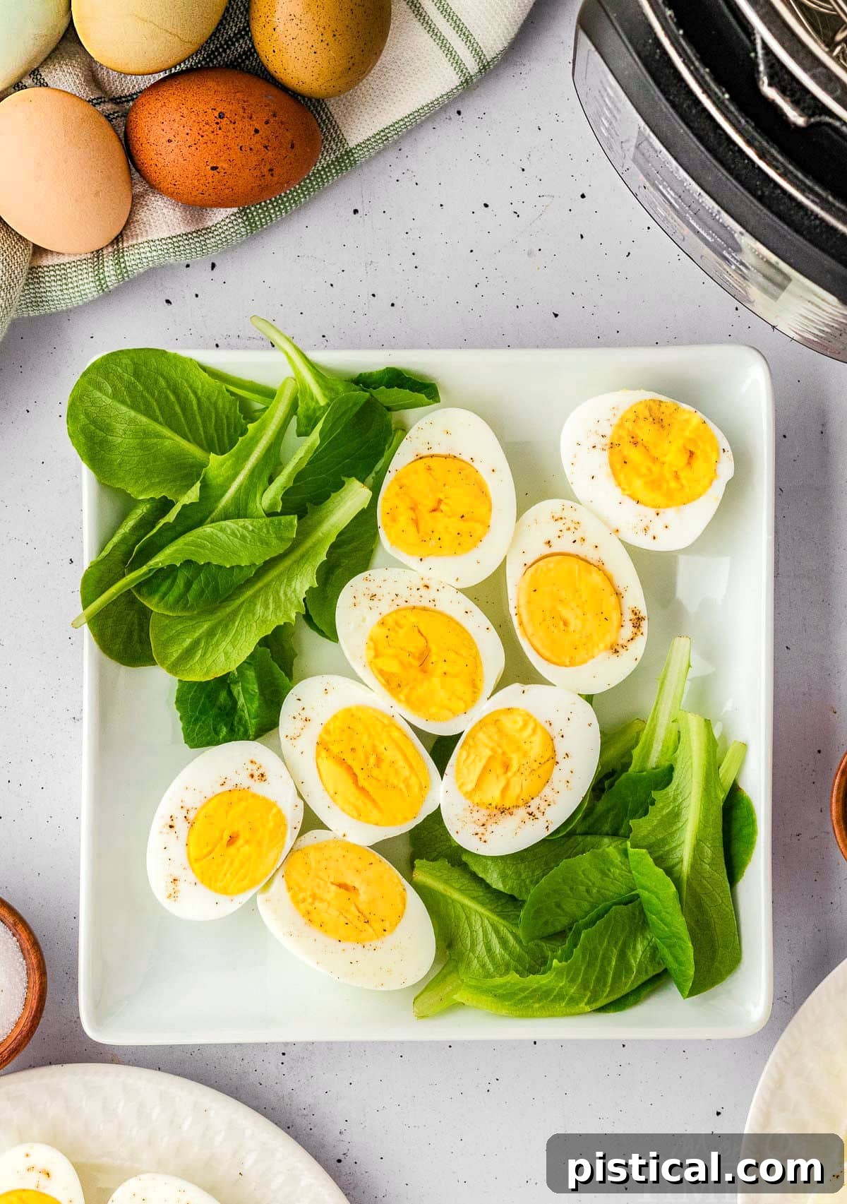 Several perfectly hard-boiled eggs, some whole and some halved, presented on a bed of fresh spinach leaves on a white plate.