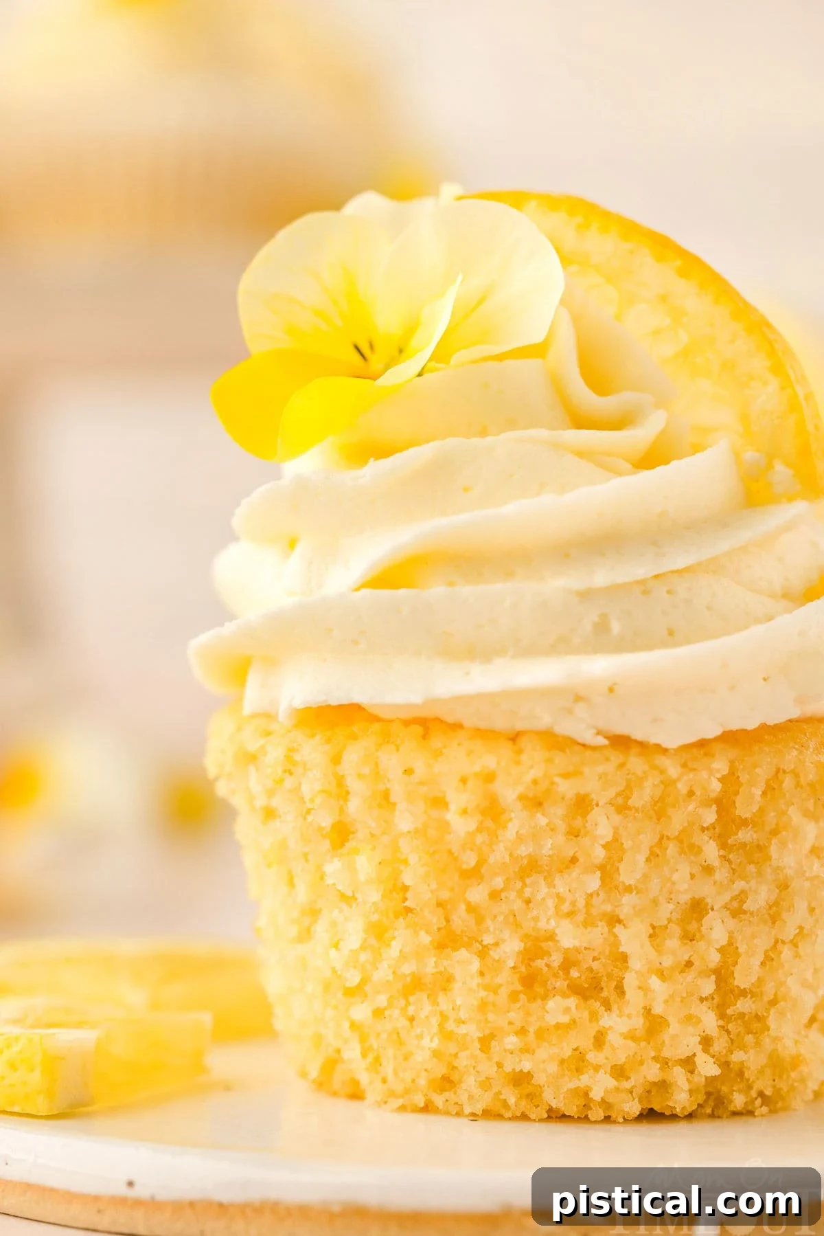 Zesty Lemon Delight Cupcakes 9 Close up side view of a lemon cupcake with a lemon wedge and flower garnish.