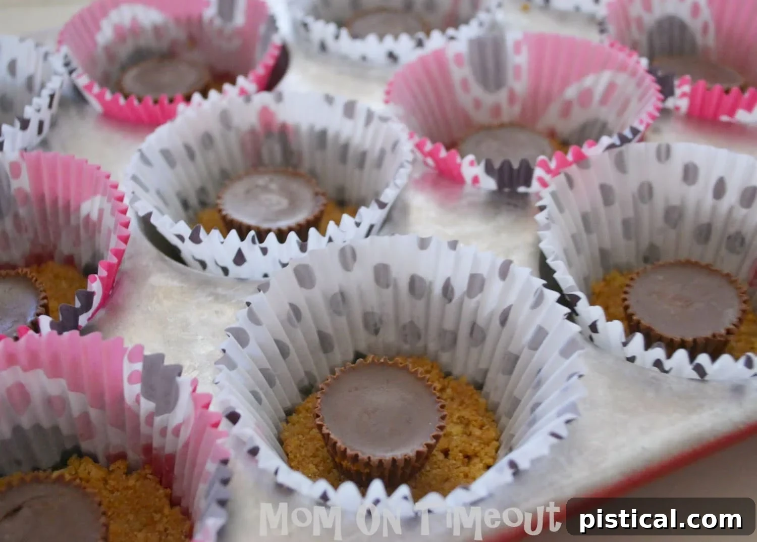 Graham cracker crust being pressed into a muffin tin, with Reese's cups added.