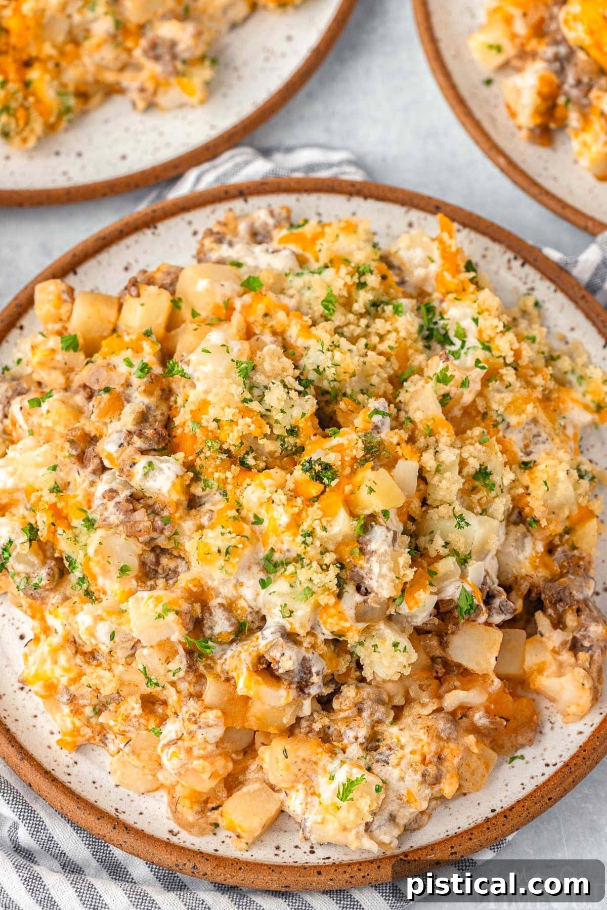 Top down view of a serving of ground beef and potato casserole on a round plate, garnished with fresh chopped parsley.