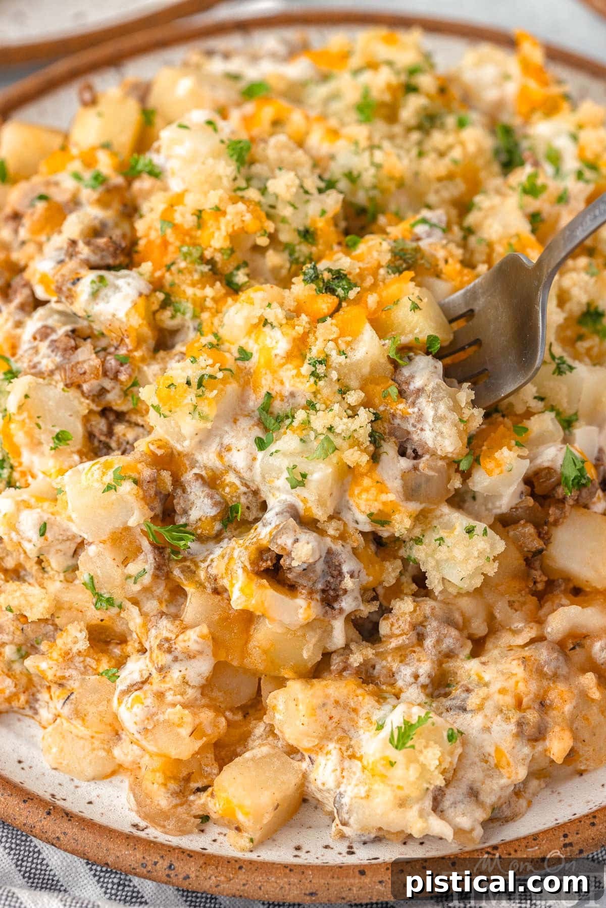 Close-up of a plated ground beef and potato casserole, with a fork digging into the cheesy layers.