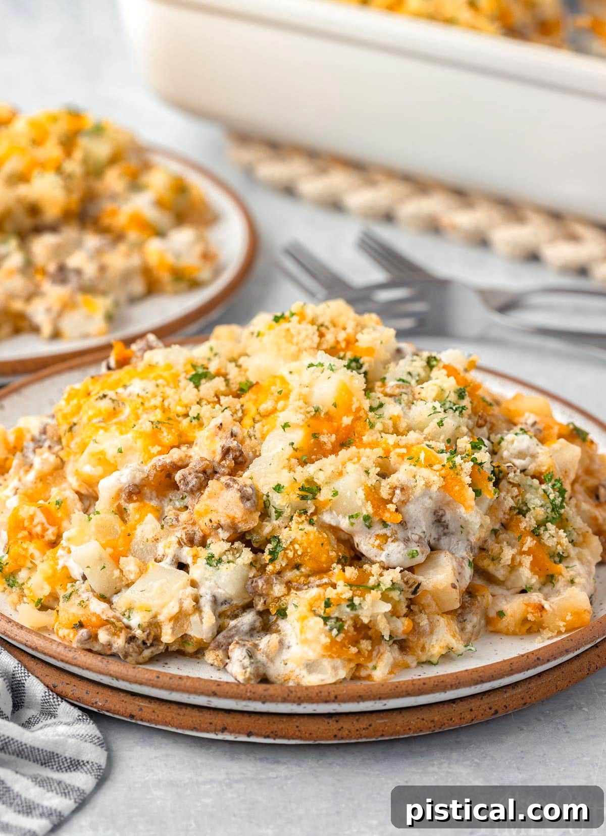 Front view of a plated serving of ground beef potato casserole on a brown-rimmed plate, with the casserole dish blurred in the background.