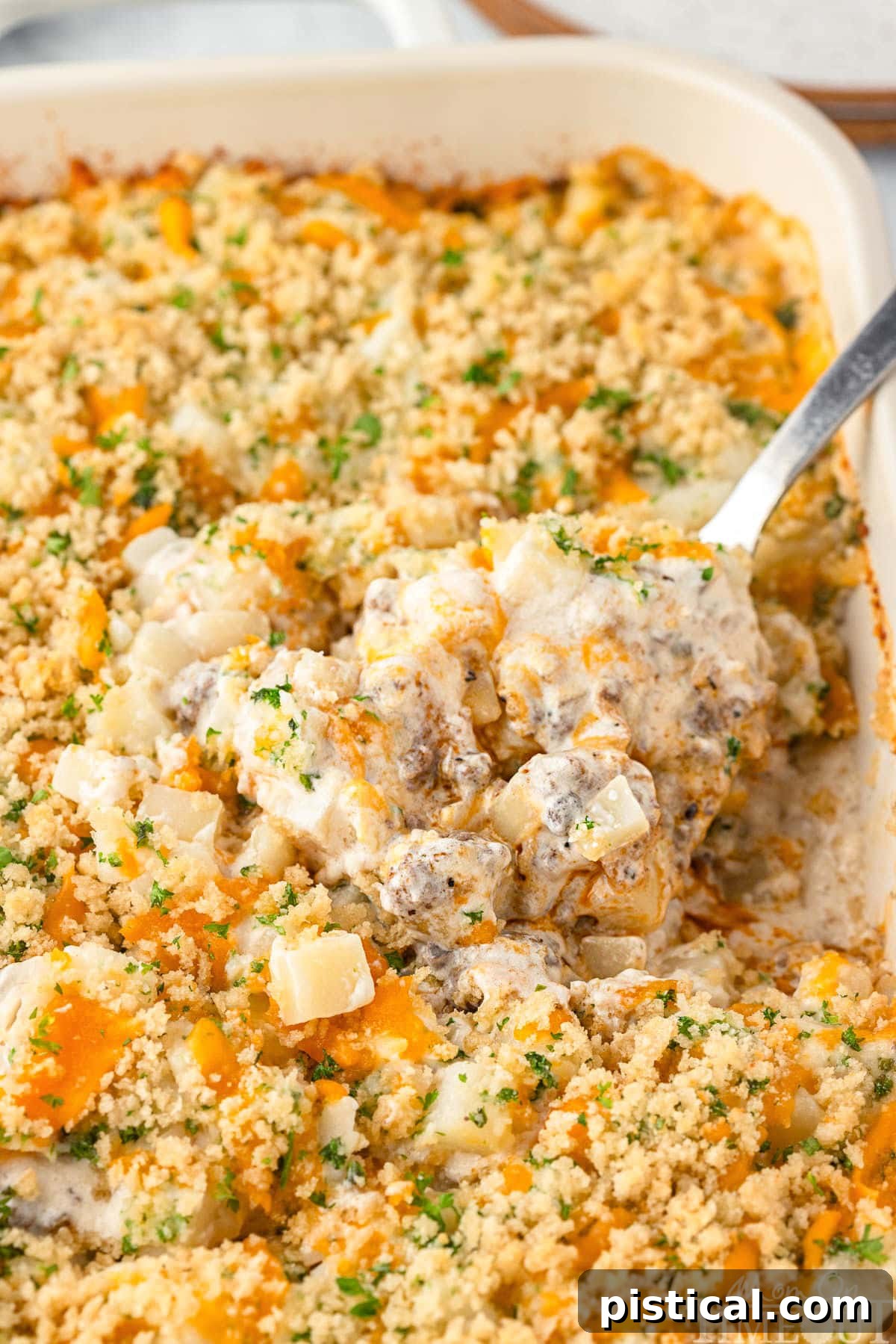 Casseroles with ground beef in a serving dish, with a large serving spoon scooping out a portion.