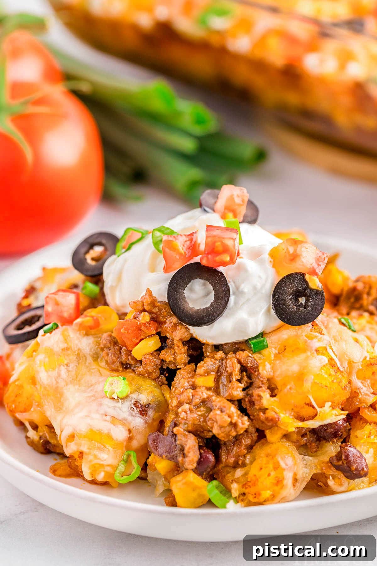 A generous serving of Mexican Tater Tot Casserole on a pristine white plate, garnished with a dollop of cool sour cream and finely sliced black olives.