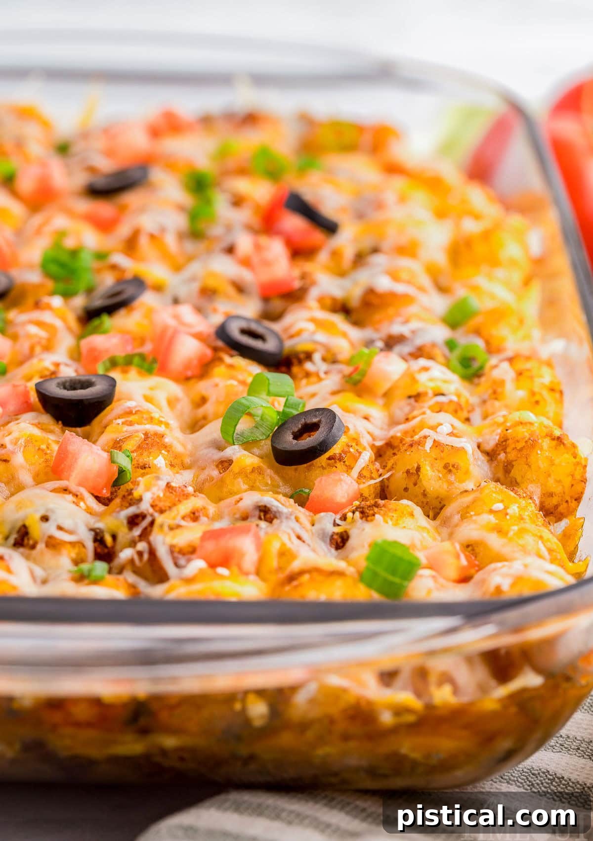 A close-up shot of the Mexican Tater Tot Casserole in a glass baking pan, highlighting the crispy golden tater tots and the rich, bubbling cheesy filling beneath.